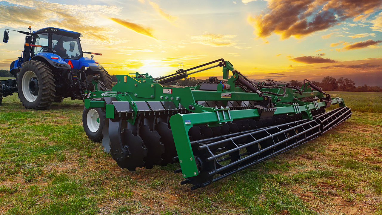 New Holland tractor towing a K-Line Ag Speedtiller Powerflex® in a paddock at sunset beneath a dramatic cloudy sky