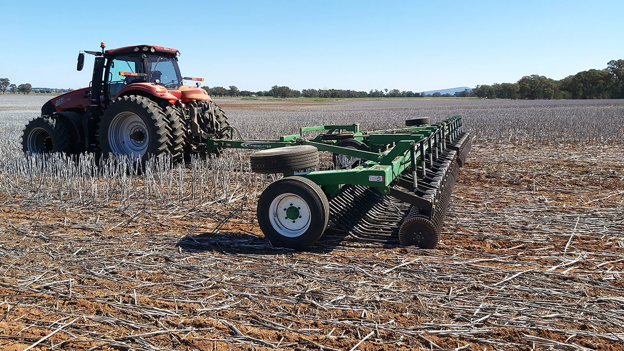 A K-Line Ag Trashcutter® being towed through a field of stubble by a Case IH tractor under a bright blue sky