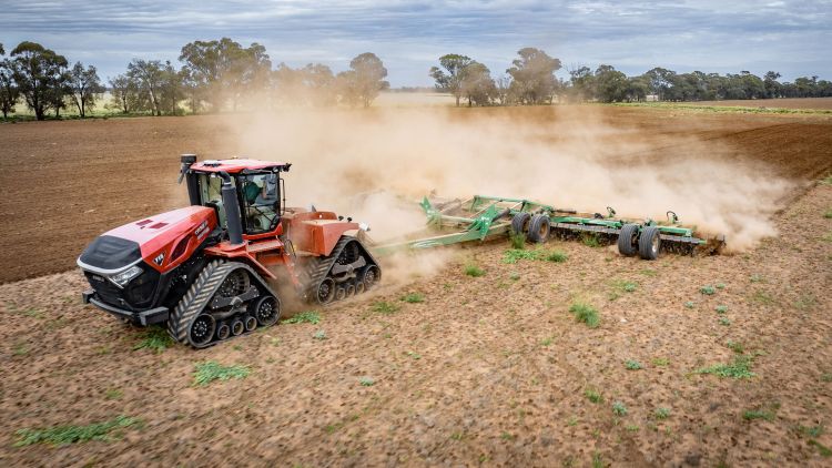 A red Case IH tracked tractor pulling a K-Line Ag Speedtiller® tillage implement through a dry paddock, raising dust under a cloudy rural sky