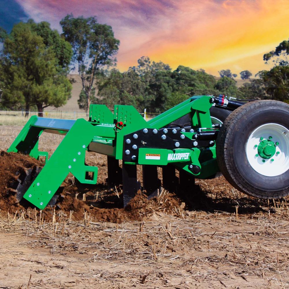 A K-Line Ag MaxxRipper working a paddock. The tynes are ripping up the brown earth and dust is trailing behind.