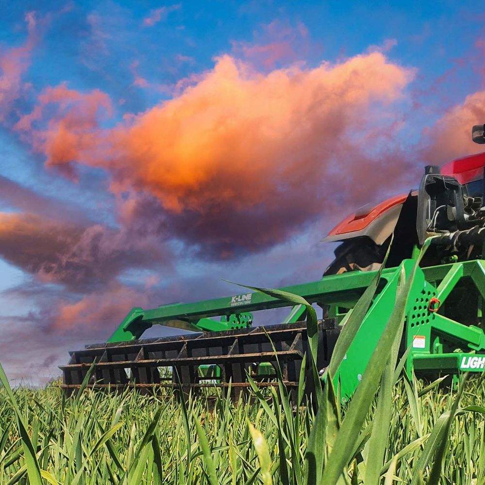 A K-Line Ag LightningRipper sitting on green grass in a field. There is a blue sky with pink fluffy clouds in the distance.